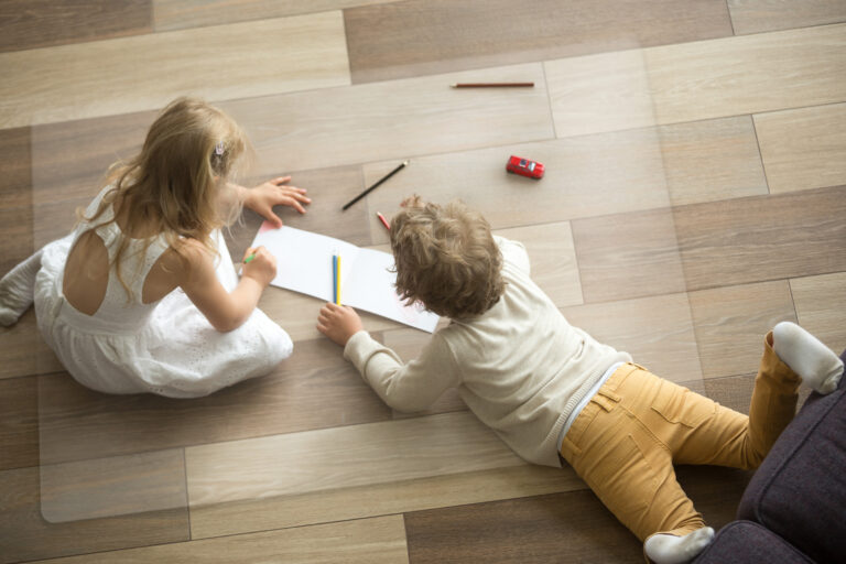 Kids sister and brother playing drawing together on wooden warm floor in living room, creative children boy and girl having fun at home, siblings friendship, underfloor heating concept, top view