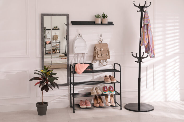 Black shelving unit with shoes and different accessories near white wall in hall. Storage idea