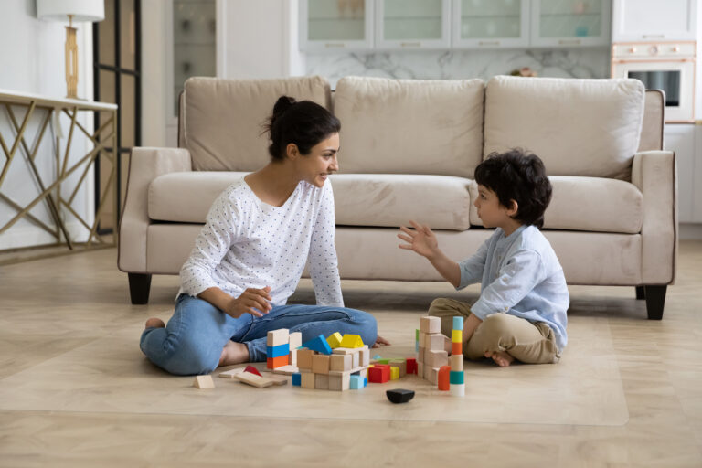 Loving young Indian mother and little son playing together on heating floor, building towers from toy construction bricks, talking, enjoying leisure, playtime, creative game. Motherhood concept